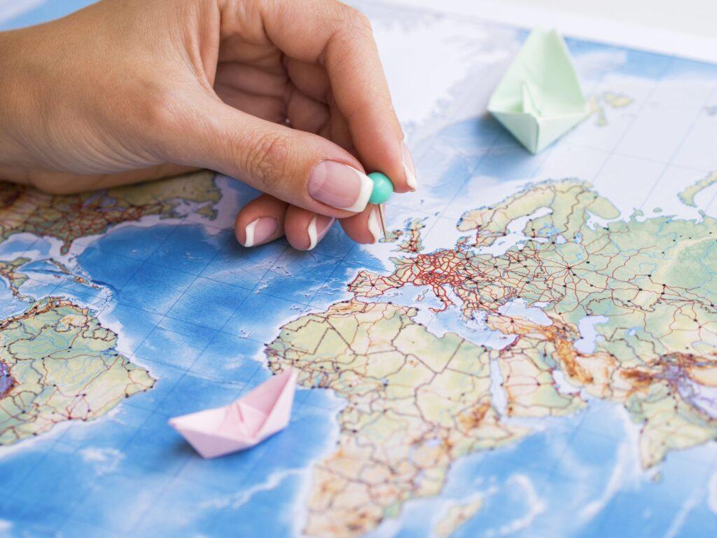 Hand placing a pin on a map of Europe, with paper boats nearby, symbolizing global business strategies and transfer pricing advantages.