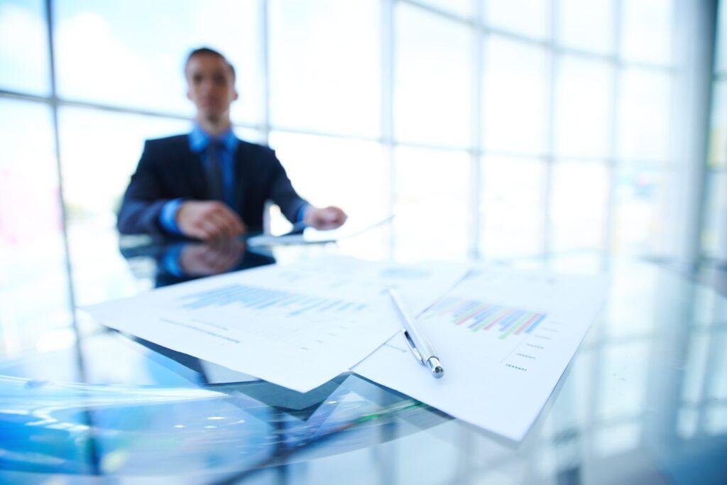 Business professional sitting at a modern glass table with financial charts and a pen, symbolizing the advantages of transfer pricing