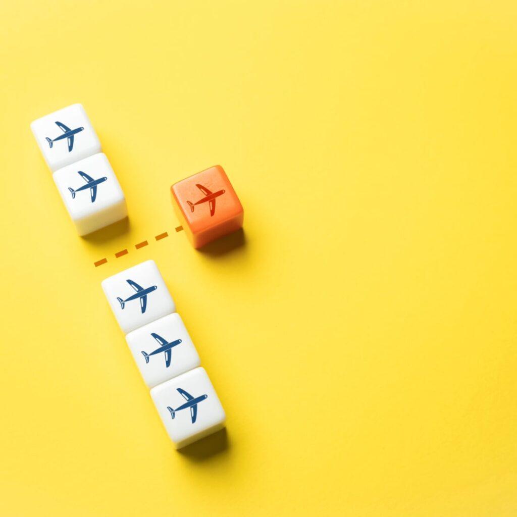 Orange cube with airplane icon breaking away from a group of white cubes with similar airplane icons, symbolizing unique transfer pricing trends