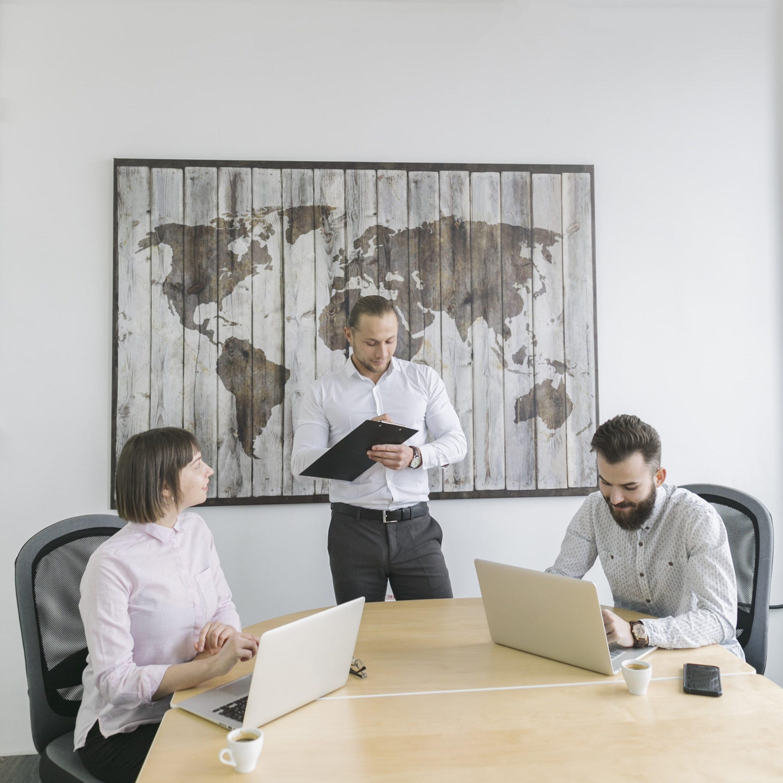 Three business professionals working on laptops and reviewing documents during an international transfer pricing meeting.